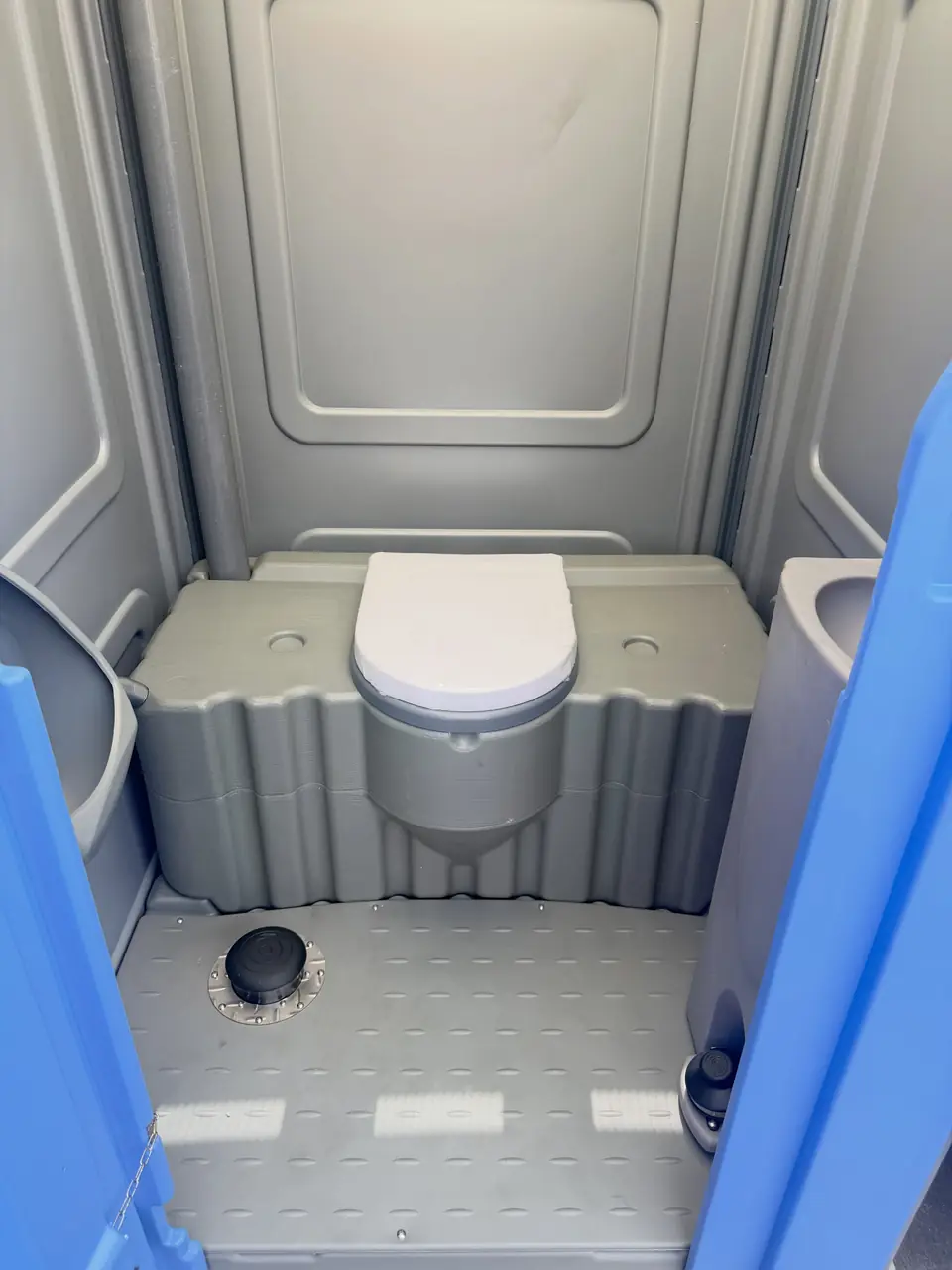 Clean porta potty interior with white toilet seat and gray floor
