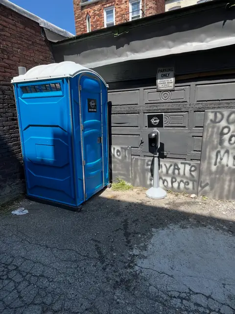 Blue porta potty placed beside a garage on a home driveway