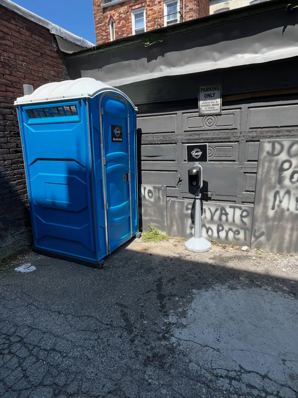 Blue porta potty placed on a driveway beside a home garage