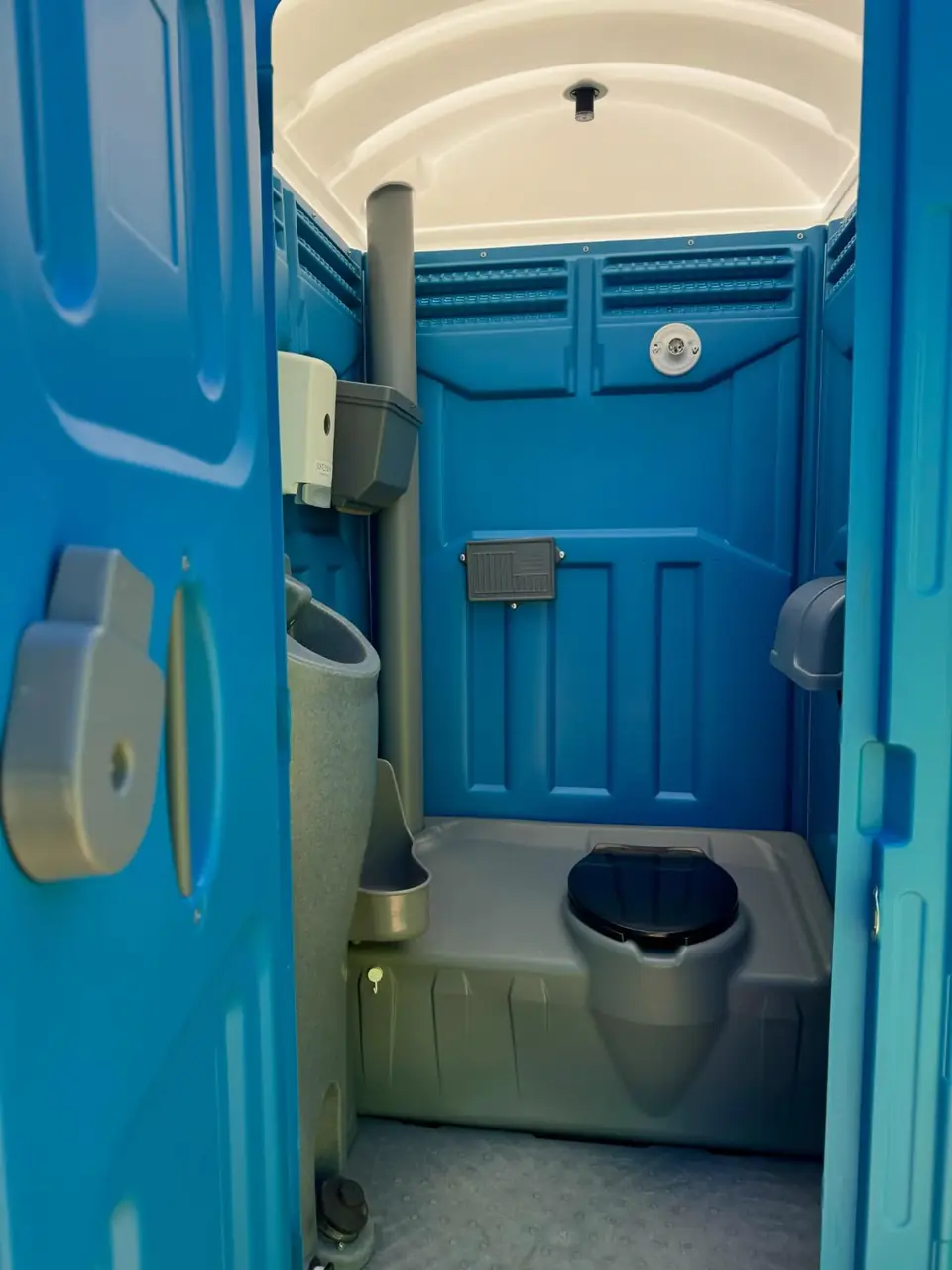 Wide porta potty interior with seat and hand sanitizer dispenser on the wall