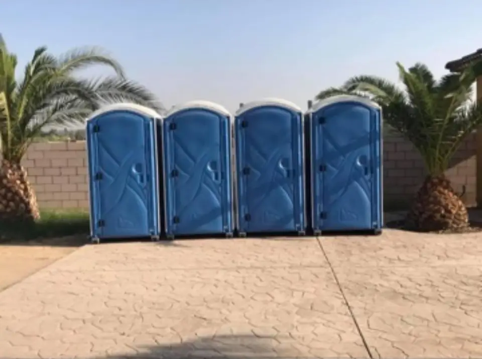 Four blue standard porta potties lined up on a paved patio